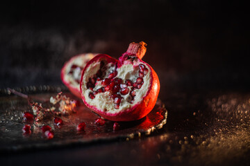 halves of pomegranate with sprinkled grains on a beautiful vintage tray on a dark background