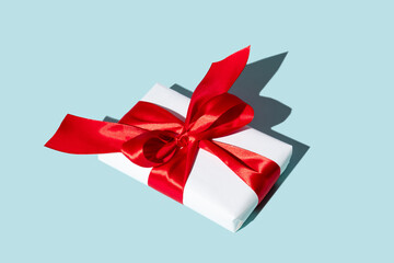 Holiday surprise. Long-distance gift. Care package. Special day congratulation. Present wrapped in white box with red ribbon bow isolated on blue background.