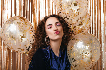 Naklejka premium Beautiful girl with pink eyeshadows winks on gold background with balloons