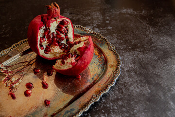 halves of pomegranate with sprinkled grains on a beautiful vintage tray on a dark background