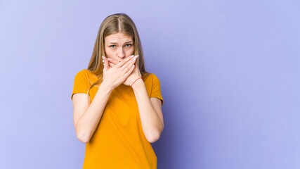 Young blonde woman isolated on purple background covering mouth with hands looking worried.
