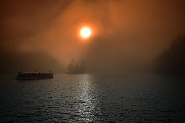 Naklejka premium Sonnenaufgang über dem nebeligen Königssee mit einem fahrenden Schiff