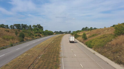 Aerial shot of truck with cargo trailer driving on motorway and transporting goods. Camera following to delivery lorry moving through country highway at sunny day. Flying over road traffic in rural