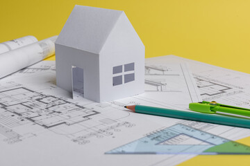 White family paper house, house projects plan and blueprints on yellow background paper. Minimalistic and simple concept, style. Vertical orientation