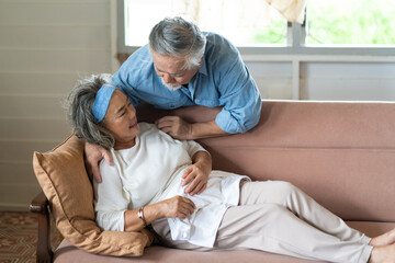 Asian Elderly couple at home. Old woman in pain lying on sofa with senior husband at home