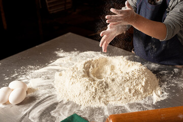 
hands of a girl kneading flour with eggs and rolling pin on steel countertop