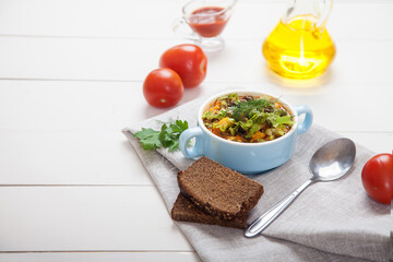 Bean and olive soup with herbs in a ceramic bowl, tomatoes, olive oil and bread on a white wooden table. Copy spaes.