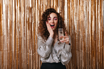 Surprised woman in silver blouse holding champagne glass