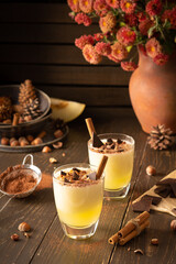 Refreshing delicious melon smoothie with cinnamon, hazelnuts and chocolate, vase of chrysanthemums and glasses of smoothie on wooden background