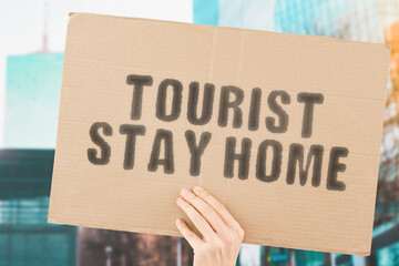 The phrase " Tourist stay home " on a banner in men's hand with blurred background. Travel. Journey. Trip. Restrictions. Prohibition. Airplane