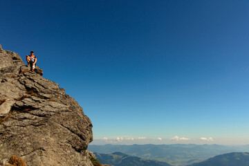 A man stands on the edge of a stone on one of the peaks of the Ukrainian Carpathians, the Montenegrin ridge, picturesque mountains on the trampled trails of the Carpathians.