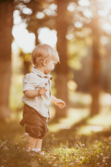 A small blond boy dressed in a vintage jumpsuit in a field at sunset