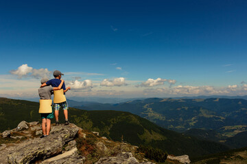 Fototapeta premium Two small children, brothers boys standing on one rocky peak, a mountain of Carpathian mountains, happy children, children on a hike.