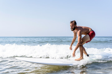 Fototapeta na wymiar Hipster man surfing with a longboard on the waves - Fit guy training with a surfboard on a slightly rough sea - Water sport, fitness and balance concept - Copy space for text, main focus on the face
