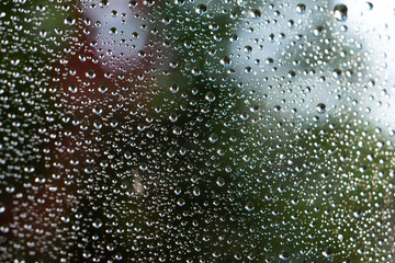 Rain water droplets on window macro close up shot colored blurred background