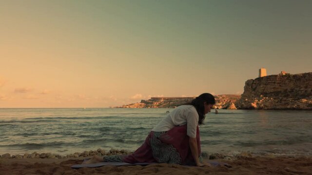 Woman in 40s practicing yoga on the sandy beach in early morning. High quality 4k footage