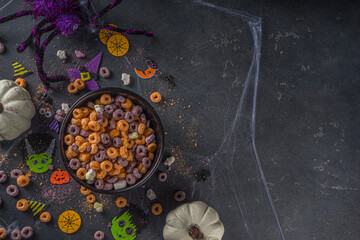 Funny halloweFunny kids cereal breakfast for halloween. Purple and orange breakfast cereal flakes with pumpkin yoghurt and halloween symbol marshmallow. On dark table with halloweenen cereal breakfast