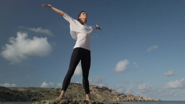 Wellbeing concept. Young caucasian woman practising yoga on the rocky beach. High quality 4k footage