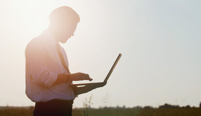 Side view of businessman holding laptop and typing keyboard standing in countryside, low angle