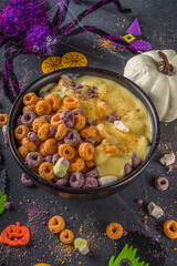 Funny halloweFunny kids cereal breakfast for halloween. Purple and orange breakfast cereal flakes with pumpkin yoghurt and halloween symbol marshmallow. On dark table with halloweenen cereal breakfast