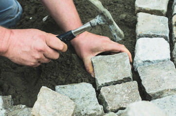 setzen eins Porphyr Pflastersteins mit dem Hammer auf einer Baustelle. Der Stein wird in Beton gesetzt. Der Hammer schwingt in Richtung des  Pflasterstein.