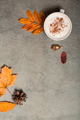 Vertical photo. A cup of coffee with cinnamon, autumn leaves, cones, acorns on a gray structural background.