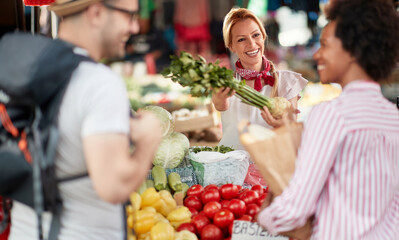 Seller woman offers fresh and organic vegetables at the green market or farmers market stall.  Young buyers choose and buy products for healthy food in grocery. All for diet healthy eating, lifestyle.