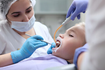 Professional dental cleaning for a child in the clinic . Children's dentist cleans the child's teeth. Photo in the interior on a light background. Pediatric dentistry.
