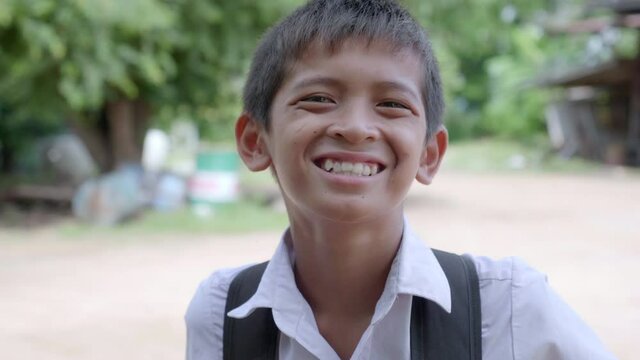 Slow motion of a smiling poor elementary school boy in Thai elementary school uniform is walking back home after school evening in the countryside of Thailand. 