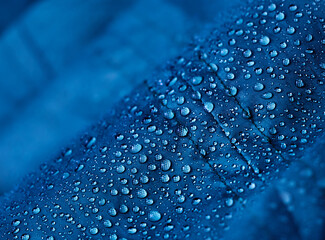 Rain water droplets on blue fiber waterproof fabric. Blue background.