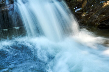 small waterfall in a mountain stream between rocks, the water is blurred in motion
