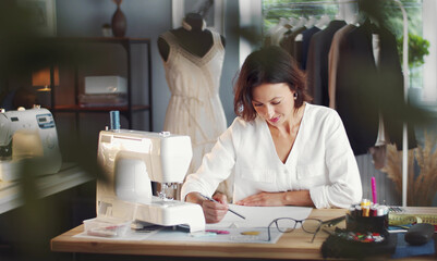 Concentrated woman fashion designer drawing sketch sitting at table in sewing workshop