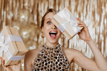 Emotional woman in elegant top covers her eyes with gift box with bow