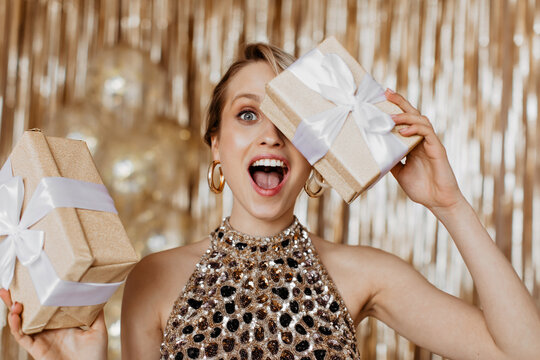 Emotional woman in elegant top covers her eyes with gift box with bow - Powered by Adobe