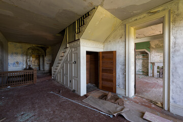 This is an interior view of a staircase with an open door underneath it at the long-abandoned and historic Dunnington Mansion in Farmville, Virginia.