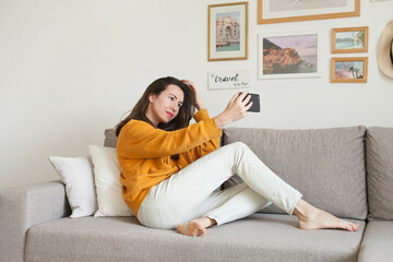 A woman sitting on a couch using mobile phone to video chat during social distancing