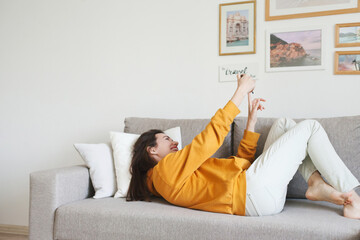 Obraz premium A woman on a couch at home using mobile phone to video chat during social distancing