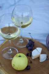 wooden stand with two glasses of champagne, grapes and camembert cheese on a white blanket in the field. picnic. 