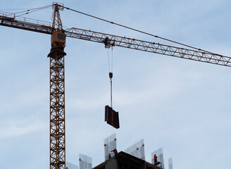 The construction of the house is in full swing. The tower crane lowers the concrete structure, and the workers coordinate where