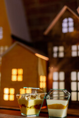 two mousse desserts with mango and chocolate on the background of decor of toy wooden houses.