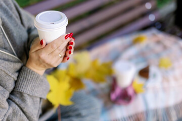 A snack in an autumn park on a bench with a blanket. A glass of coffee in the hands of a woman.