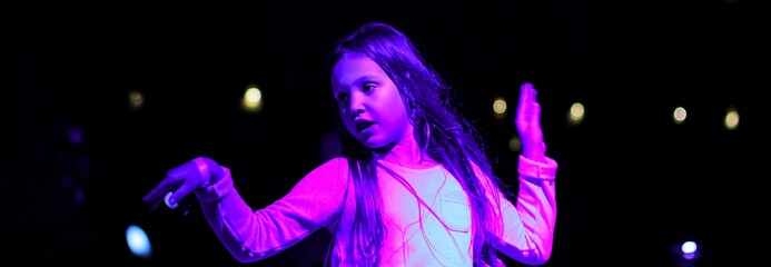 Blurred beautiful emotional young girl dancing in neon light. Trendy color banner.