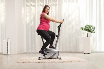 Pregnant woman in a pink top riding an exercise bike at home