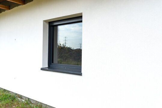A newly applied layer of white silicone plaster on the wall of the house, visible window in anthracite.