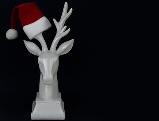 white deer in Santa hat on dark background, minimal creative concept of Christmas and New Year