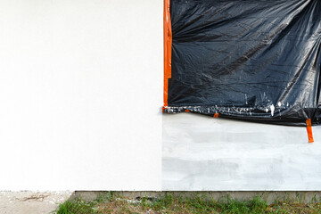 A newly applied layer of white silicone plaster on the wall of the house, the window is secured...