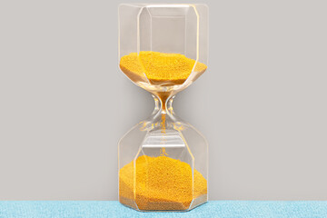 Transparent glass hourglass with falling golden yellow sand - close-up. Countdown time