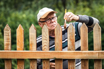 Senior man painting wooden fence in garden