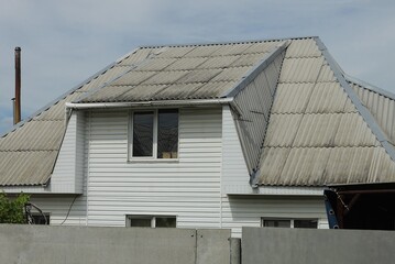 white attic of a private house with windows under a gray slate roof on the street behind a fence against the sky
