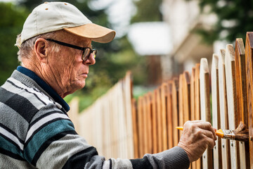 Senior man painting wooden fence